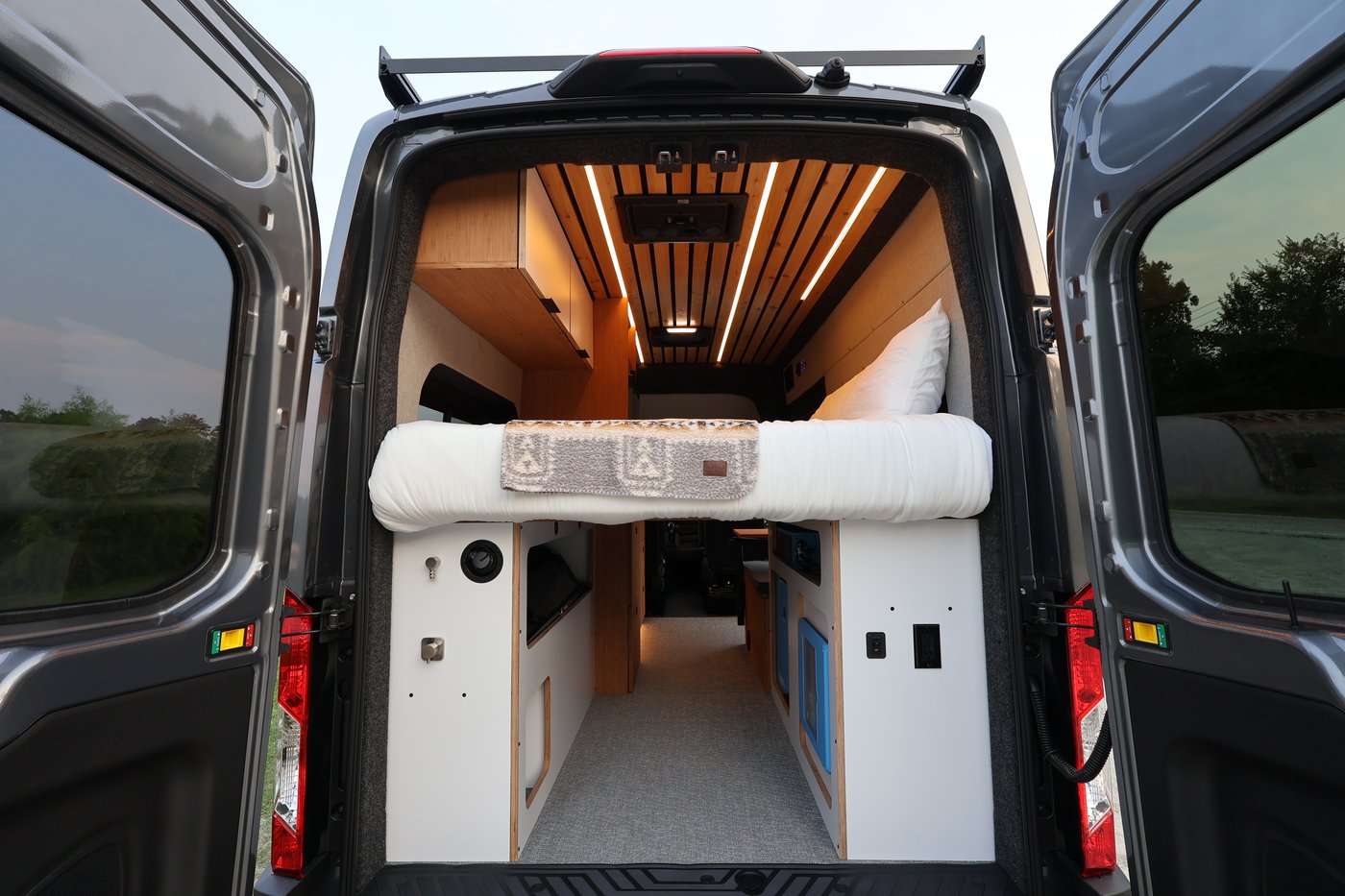 Rear view of the Aire camper van with doors open, showing the bed, water and electrical cabinets, and cedar slatted ceiling